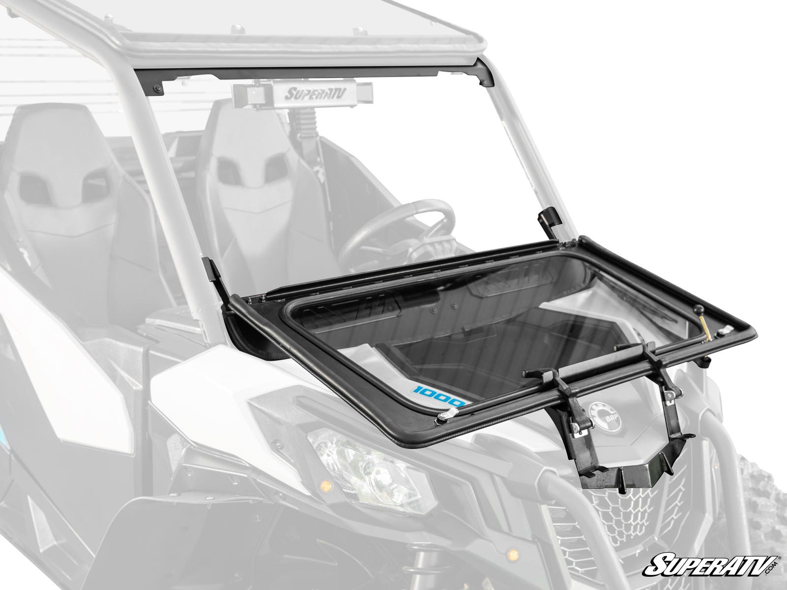 A close-up of the Can-Am Maverick Trail Flip Down Glass Windshield, partially open and attached to a white off-road utility vehicle. Hinges, locking mechanisms, seats, and the steering wheel are visible in the background.