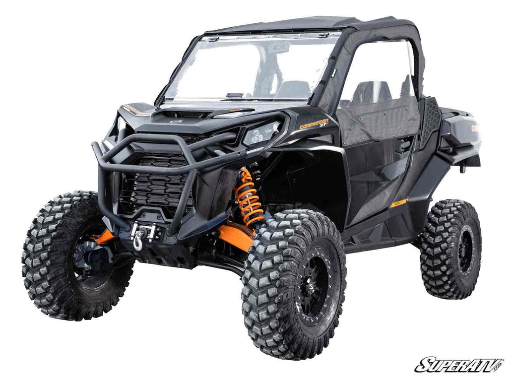A rugged black off-road side-by-side with a Can-Am Commander 3 Lift Kit, large knobby tires, orange suspension springs, front winch, clear windshield, and partial doors. SuperATV logo appears in the bottom right corner.