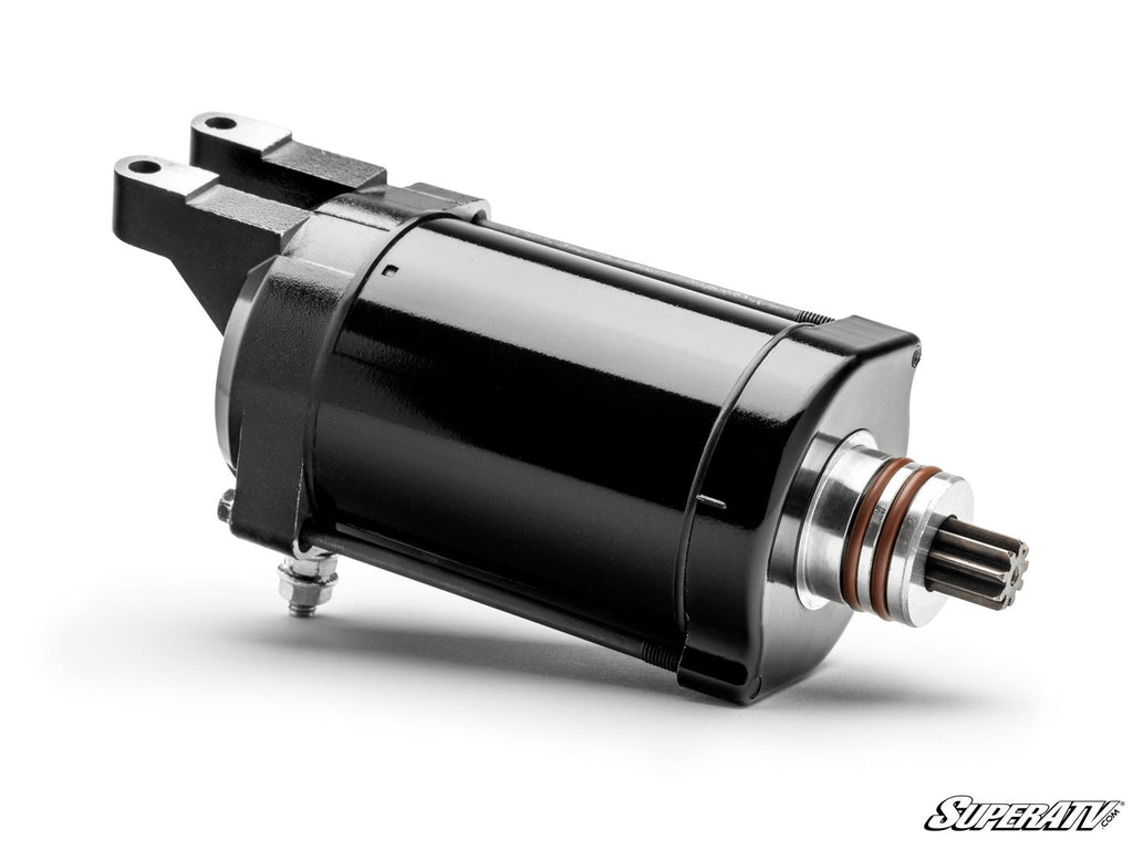 The Up & Running Can-Am Maverick X3 Starter is a black and silver electric starter motor with a cylindrical body, visible gear, mounting brackets, and metal connector. It lies on a white background with the SuperATV logo in the lower right corner.