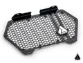 The Assault Industries Can-Am Maverick R Hellfire V2 Front Grille features a black, hexagon-patterned metal design with mounting brackets and a geometric silver emblem. It sits on a white background with a matching logo in the lower right corner, showcasi