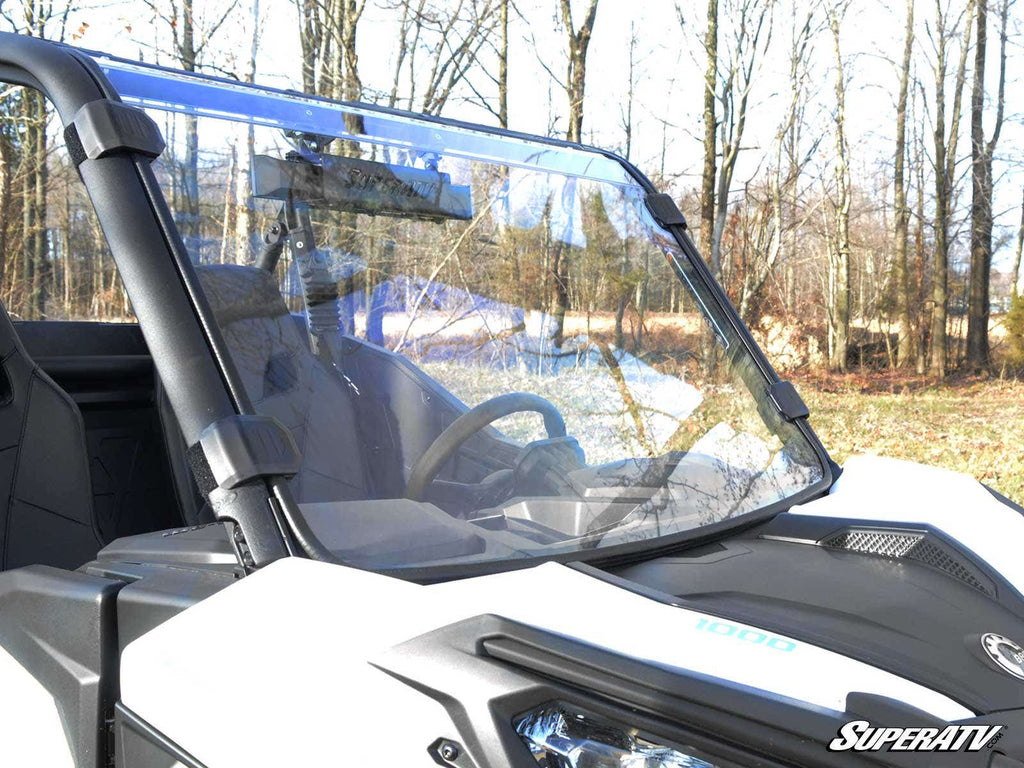 A Can-Am Maverick Trail Full Windshield is installed on a white off-road utility vehicle parked outdoors, surrounded by leafless trees and brown grass. The SuperATV logo appears in the bottom right corner.