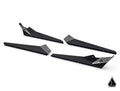 Four matte black Assault Industries Can-Am Maverick X3 MAX Rock Sliders with a geometric honeycomb pattern and logo on one end are arranged diagonally on a white background. A small triangular black-and-white logo appears in the lower right corner.