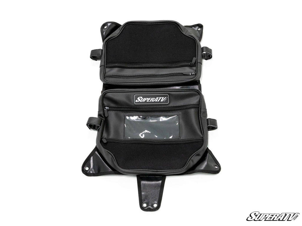 The Can-Am Maverick X3 Overhead Bag is black with multiple zippered compartments, mesh pockets, a clear window, and mounting flaps. Laid open, its interior organization and the SuperATV logo on two pockets are visible.