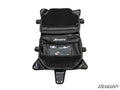 The Can-Am Maverick X3 Overhead Bag is black with multiple zippered compartments, mesh pockets, a clear window, and mounting flaps. Laid open, its interior organization and the SuperATV logo on two pockets are visible.