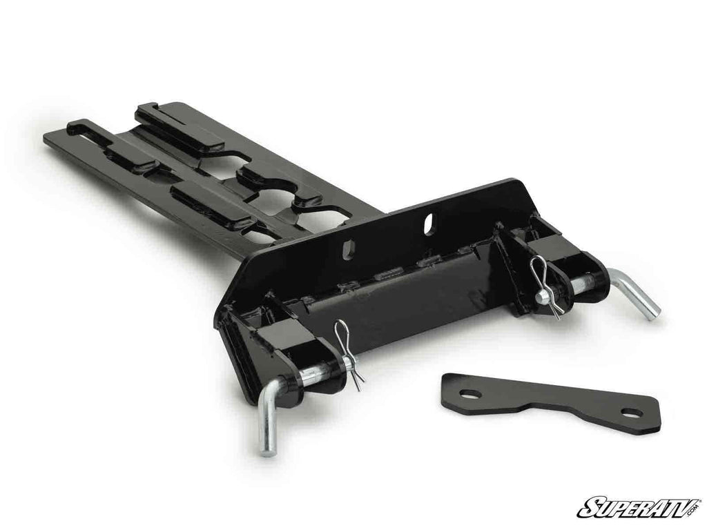 The Can-Am Maverick X3 Plow Pro Snow Plow Mount is a black metal plate with two large pins secured by clips, hardware slots, an extra flat bracket, and the SuperATV logo in the lower right corner on a white background.