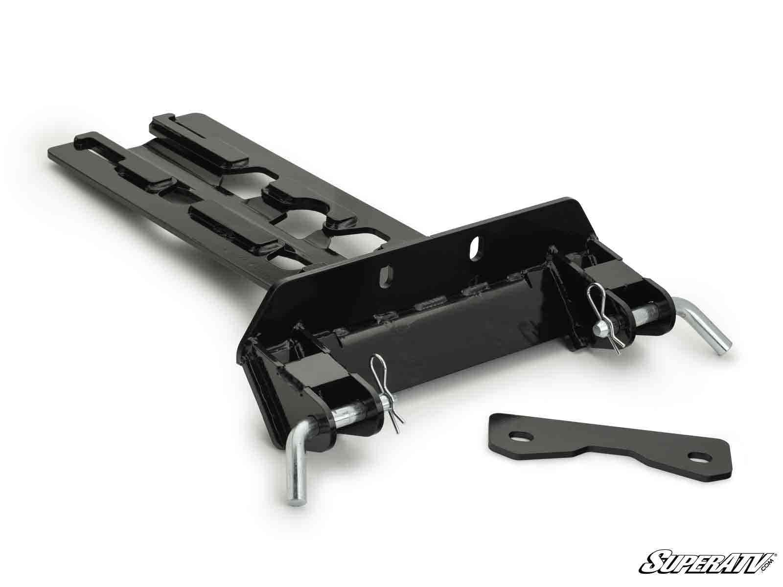 The Can-Am Maverick X3 Plow Pro Snow Plow Mount is a black metal plate with two large pins secured by clips, hardware slots, an extra flat bracket, and the SuperATV logo in the lower right corner on a white background.
