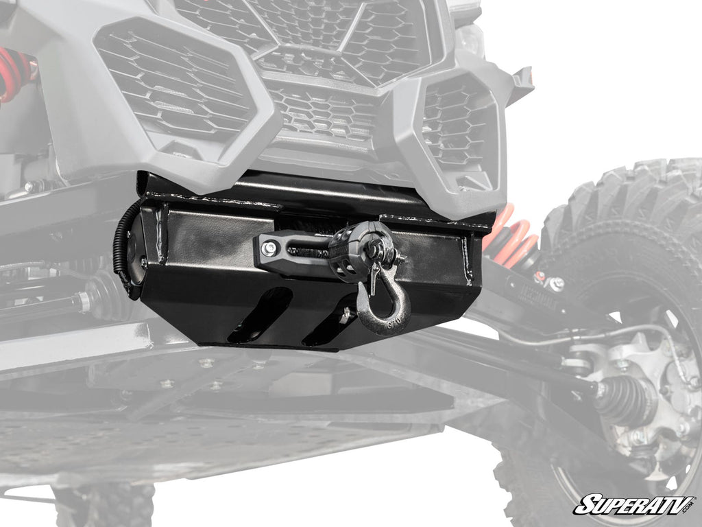 Close-up of a Can-Am Maverick X3 Ready-Fit Winch mounted under the front of an off-road vehicle with rugged suspension, red coil springs, and a black protective winch housing. The SuperATV logo is shown in the bottom right corner.