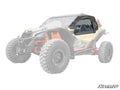 A Can-Am Maverick X3 in yellow and black features Primal Soft Cab Enclosure Upper Doors with clear windows over the cab, contrasting with the vehicle’s faded body. The SuperATV logo appears in the lower right corner.