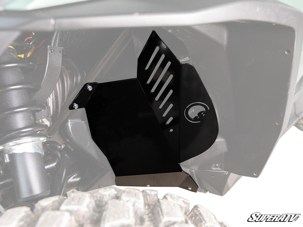 A close-up of a Can-Am Commander 1000 Inner Fender Guard shows its black metal build with slotted vents and a circular cutout installed in the wheel well. Tire tread, suspension, and the SuperATV logo are also visible.
