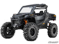 A Can-Am Maverick Sport with a 6 Lift Kit features black off-road styling, oversized mud tires, orange suspension springs, a roll cage, sturdy front bumper, closed doors, and a partially open windshield. SuperATV logo shown bottom right.