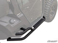 Close-up of Can-Am Defender Heavy Duty Nerf Bars, black tubular metal with an angular step plate, installed on an off-road vehicle showing a ROTAX label, clear door, and rugged tire.