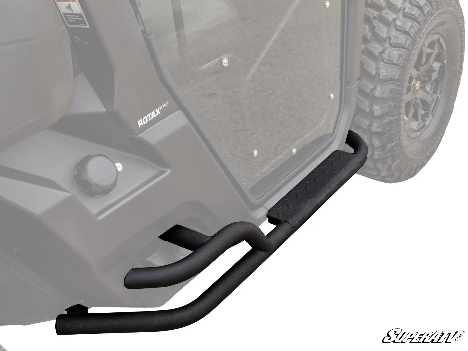 Close-up of Can-Am Defender Heavy Duty Nerf Bars, black tubular metal with an angular step plate, installed on an off-road vehicle showing a ROTAX label, clear door, and rugged tire.