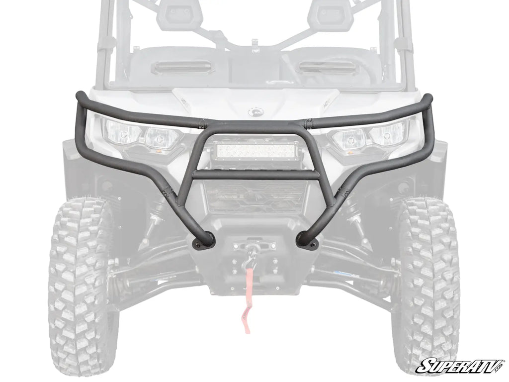 The Can-Am Defender Front Bumper, a black, heavy-duty bumper with tubing and a central protective plate, is mounted on an off-road vehicle. It has a winch opening for rugged terrain. The SuperATV logo appears in the lower right corner.