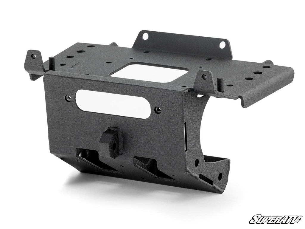 The Can-Am Maverick R Winch Mounting Plate is a black, rectangular metal bracket with cutouts and flanges for secure attachment. It features a matte finish and is pictured angled on white with the SuperATV logo in the bottom right corner.