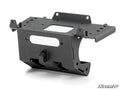 The Can-Am Maverick R Winch Mounting Plate is a black, rectangular metal bracket with cutouts and flanges for secure attachment. It features a matte finish and is pictured angled on white with the SuperATV logo in the bottom right corner.