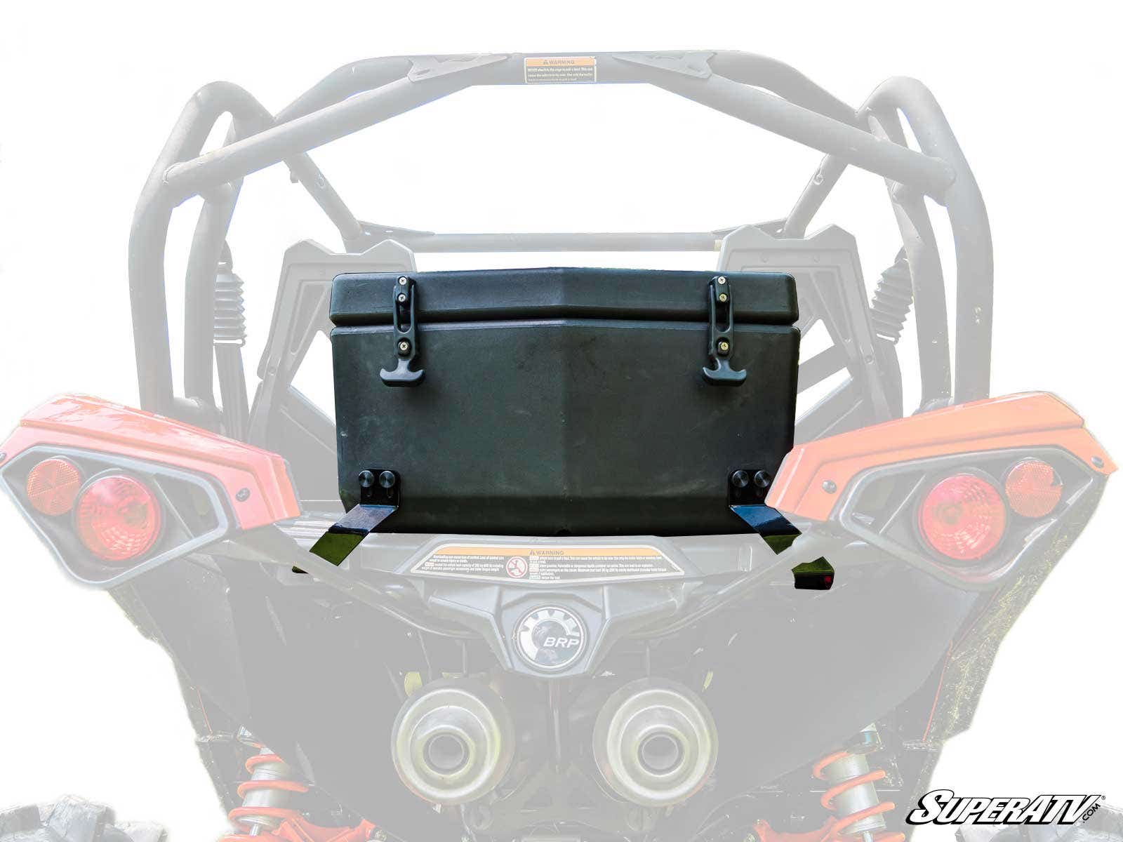 A Can-Am Maverick Cooler / Cargo Box with two latches is mounted on the rear rack of a red off-road side-by-side vehicle. The faded white background features the SuperATV logo in the bottom right corner.