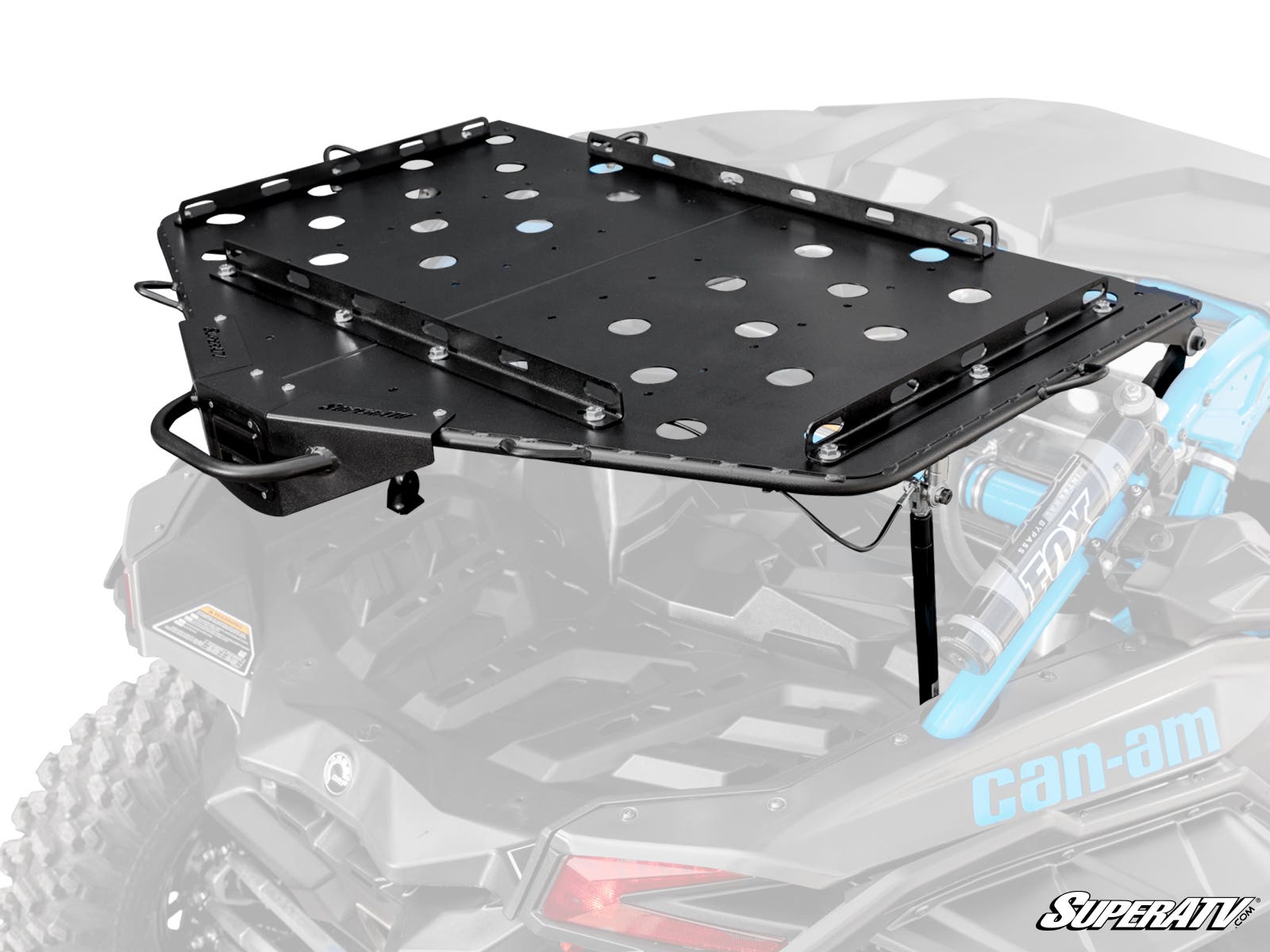 The Can-Am Maverick X3 Cargo Rack Alpha, a black metal rack with circular cutouts, is mounted on the rear of a Can-Am off-road vehicle. It features side supports, attachment points, and the SuperATV logo with visible rear suspension below.
