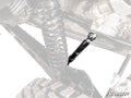 Close-up of a Can-Am Maverick R Sway Bar Shock with a large coil spring, black shock absorber, and rugged tire. Mostly black and gray parts; “SuperATV” logo at bottom right. Some areas are desaturated for emphasis.