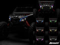A Can-Am Maverick X3 with black body and red suspension is shown in low light, featuring Fang Lights headlights in eight colors: white, blue, cyan, green, purple, orange, red, and yellow. SuperATV appears in white text at the bottom right.