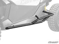 Can-Am Maverick X3 Tree Kickers are mounted along the side of an off-road vehicle, protecting the lower body and frame. The grayscale image highlights their angular, tubular design, with the SuperATV logo in the bottom right corner.
