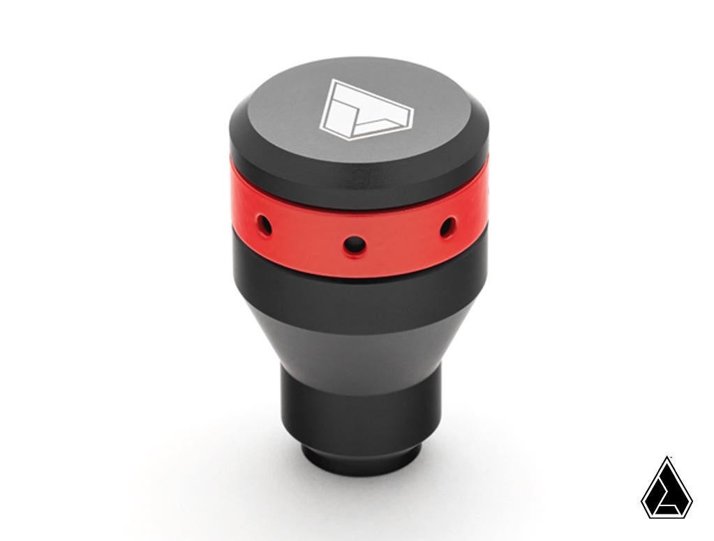 A black and red Assault Industries Stealth Shift Knob for Can-Am Maverick X3 sits on a white background. The tapered knob features a white geometric logo on top, circular holes in the red section, and a small triangular logo at the bottom right.