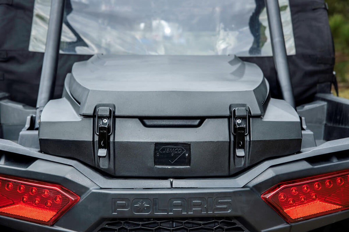 Close-up of a black JEMCO XP II UTV Rear Cargo Box mounted on a Polaris RZR XP 1000, featuring the Jemco logo and “POLARIS” embossed below red angular tail lights. The background appears slightly blurred.