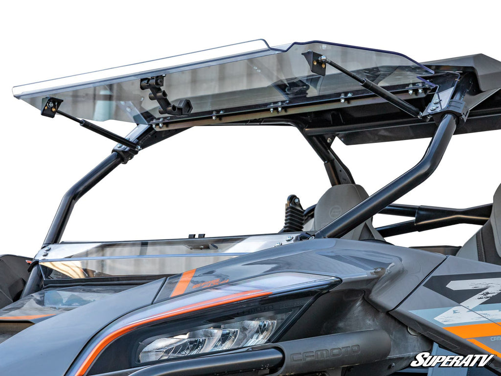 A close-up of a CFMOTO ZForce 950 with a scratch-resistant flip windshield, showing an orange stripe, sturdy black frame, visible interior seats and roll cage. SuperATV branding appears in the bottom right corner.