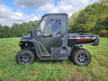 A black CFMoto UForce 1000 with HDPE hard doors and large off-road tires is parked on grass, surrounded by green trees under a partly cloudy sky.