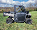 A CFMoto UForce 1000 with Soft Upper Doors, featuring a camo pattern and black cab enclosure, sits on grass in an open field. Large off-road tires stand out, while trees and hills are visible under a partly cloudy sky.