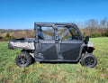 A CFMoto UForce 1000XL with upper soft front and rear doors, featuring large rugged tires and a cargo bed, is parked on grass with leafless trees and a clear blue sky in the background.