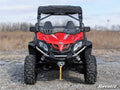 A CFMOTO ZForce 500 with a Scratch-Resistant Full Windshield is parked on rocky ground amid dry grass and bare trees. It has large tires, black accents, a winch, roof, and SUPERATV branding. The sky above is partly cloudy.