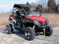 A red and black off-road CFMOTO ZForce 500 with rugged tires, roof, winch, and a Scratch-Resistant Half Windshield sits on rocky ground before dry grass and leafless trees. “SuperATV” is in white text at the lower right of the image.