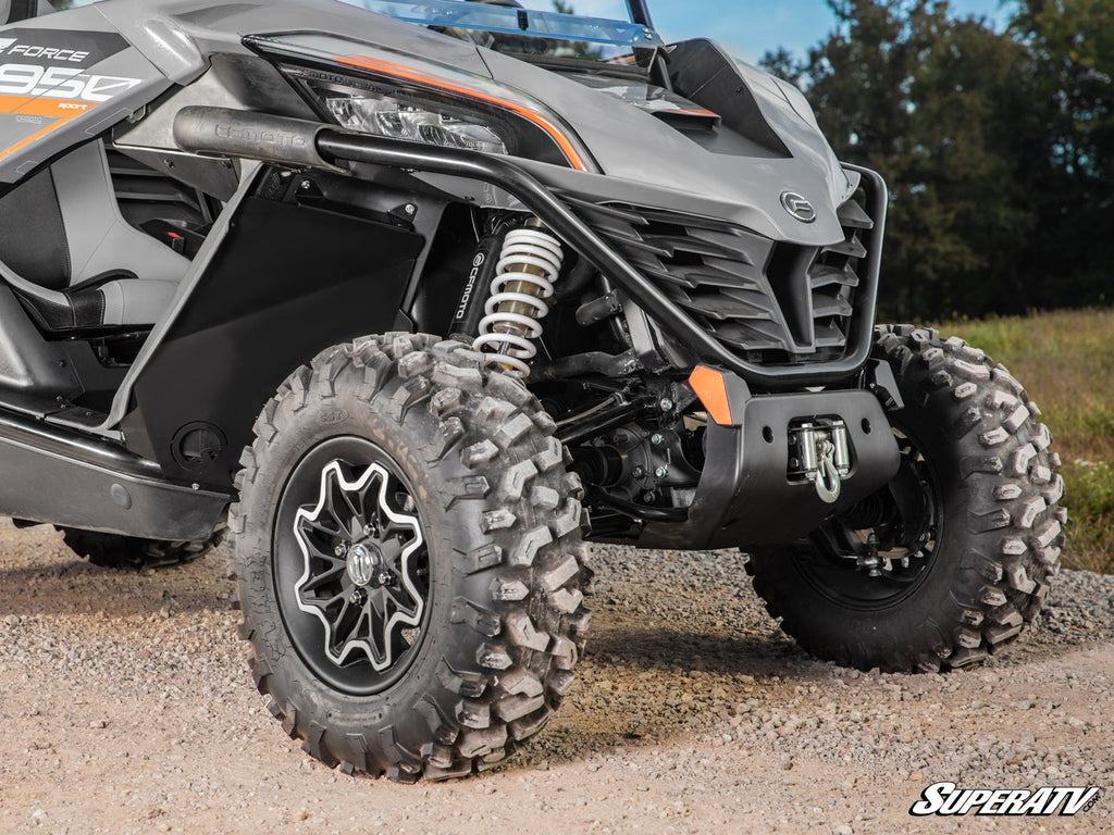 Close-up of the front wheel and suspension system of a rugged vehicle equipped with CFMOTO ZForce 950 Inner Fender Guards. Featuring aggressive tires, visible springs, and a gray body with black details, its parked on a gravel path near grass and trees.