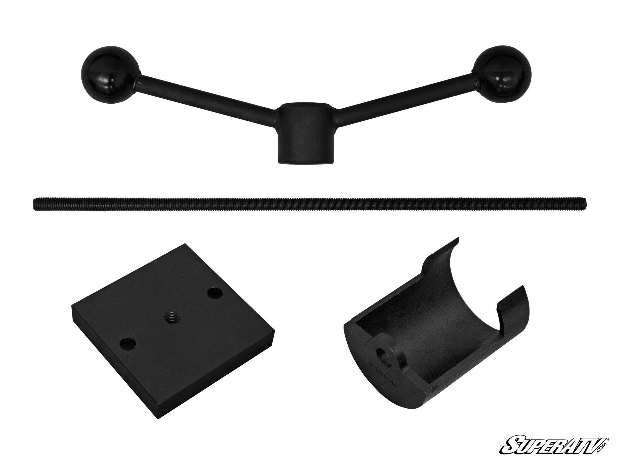 Five black metal parts from the Clutch Compressor Tool are arranged on a white background: a Y-shaped arm, threaded rod, rectangular plate, half-cylinder clamp, and square plate. SuperATV logo appears at the bottom right.