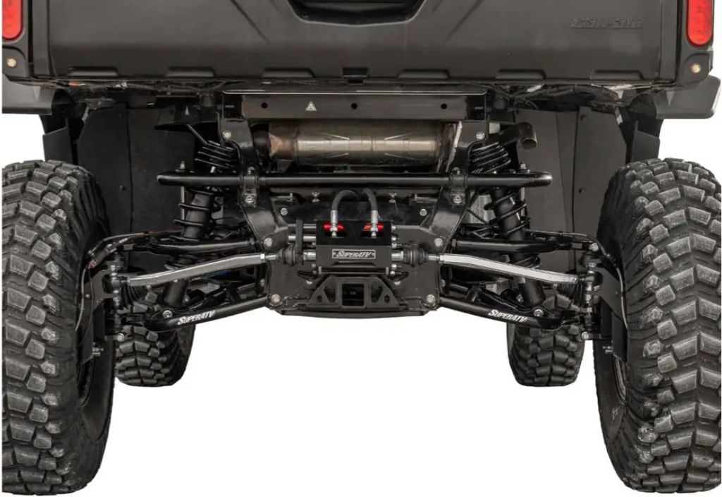 Close-up rear view of the Can-Am Defender HD10 Ride System Rear Steering Kit, highlighting its large rugged tires, heavy-duty black shocks and springs with visible branding, and a reinforced axle that showcases durability and advanced engineering.
