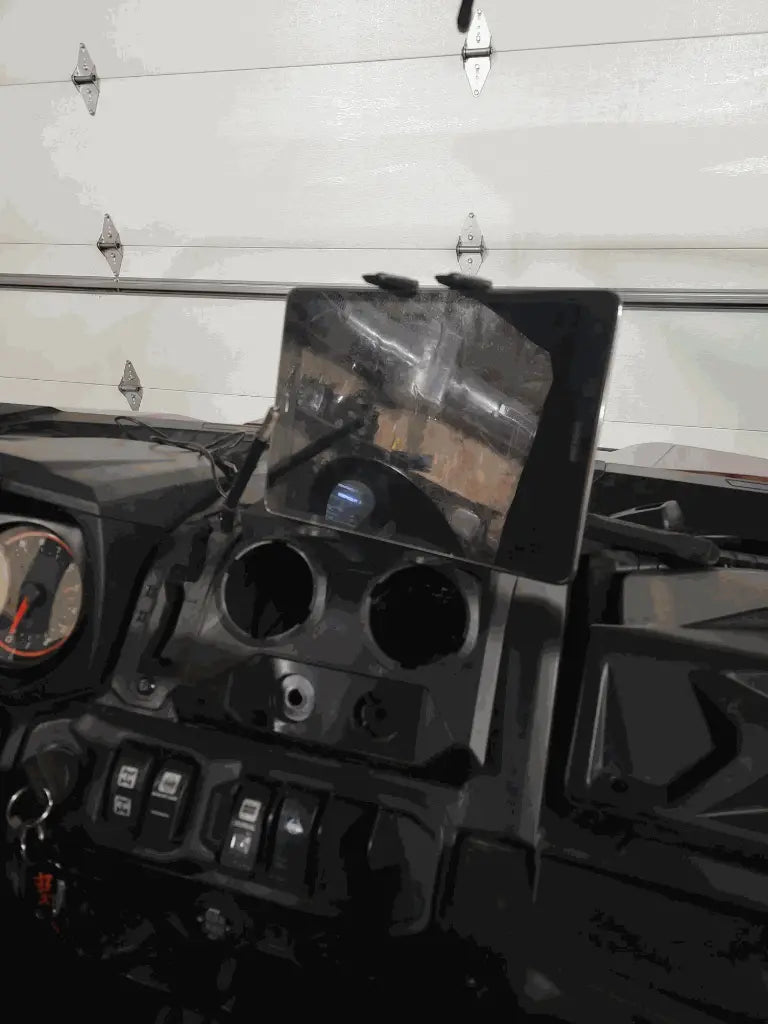 A Defender Limited & Cab Tablet/Phone Holder Center Insert is mounted above two empty circular openings on a dashboard with switches and gauges, with an iPad reflecting the white garage door background.
