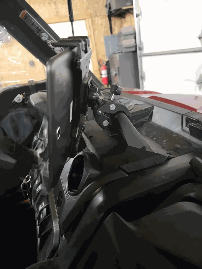 A close-up of a rugged vehicle dashboard features the Defender Limited & Cab Tablet/Phone Holder Center Insert, mounting a black tablet near the windshield. Visible controls, vents, a wooden wall, and closed garage door complete the scene.