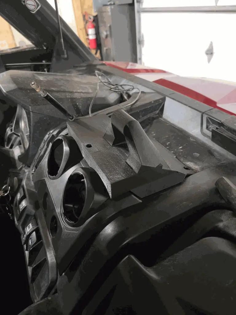 A close-up shows the Defender Limited & Cab Tablet/Phone Holder Center Insert, a black 3D-printed mount above the air vents on a rugged vehicle dashboard, with visible wires, partial steering wheel and controls, plus garage light in the background.