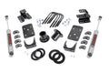 The Lowering Kit | Spr Drop | 1-2FR | 4RR for Chevy/GMC 1500 (07-13) is displayed on a white background, featuring two gray shocks, black brackets, U-bolts, spacers, washers, nuts, and curved mounting plates arranged symmetrically.