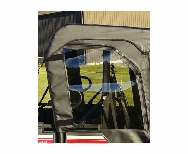 A close-up of a Kawasaki Mule Pro-FXT | DXT shows Soft Upper REAR Doors with a clear plastic window reflecting outdoor scenery. The interior reveals parts of the frame, seats, and steering wheel.