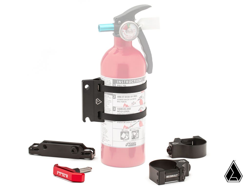 The Assault Industries Quick Release UTV Fire Extinguisher Mount is shown upright with black mounting brackets, metal clamps, a bracket, and a red Allen wrench. Visible are instructions, labels on the extinguisher, and a geometric logo in the bottom right