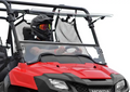 A person in a black helmet and goggles drives a red Honda off-road vehicle with a Honda Pioneer 700 Scratch Resistant Flip Windshield, mesh safety net, windshield bar, rugged design, and visible Honda logo. The background is plain white.