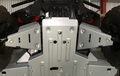 A close-up of the underside of a Honda Pioneer 1000 (2022+) shows silver alloy front A Arm Guards bolted in place, protecting the chassis. Rugged tires are visible on either side, with some framework above.