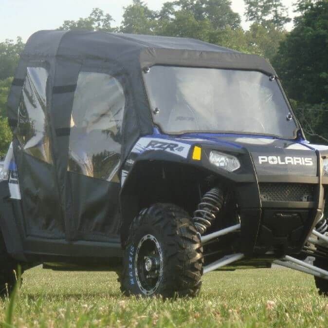 A Polaris Rzr Xp 900/800 4 Seater with a full enclosure for existing windshield, featuring black and blue canvas, transparent side windows, and rugged tires, is parked on grass amid green trees under a clear sky.