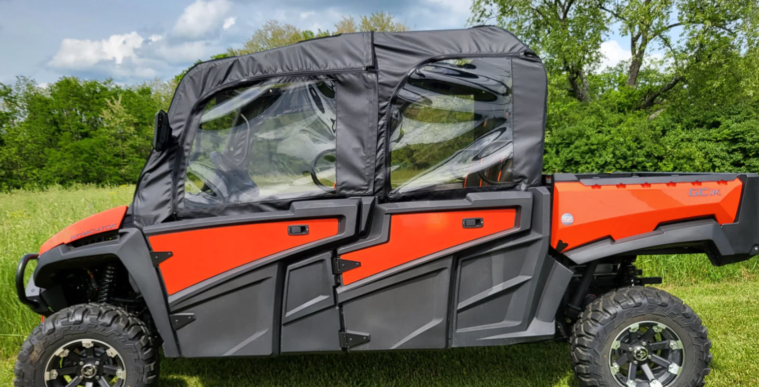 A red and black Intimidator GC1K 6-Seater with soft doors is parked on grass, featuring a clear plastic and fabric enclosure, large rugged tires, a rear cargo bed, and four rows of seats. Green trees and a cloudy sky fill the background.