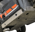 Close-up of the Polaris General 4 Rock Slider Set (2020-2024) installed on an off-road vehicle, featuring a durable silver metal skid plate with bolts and circular holes. A rugged tire and part of the body with orange and white stripes are also visible.