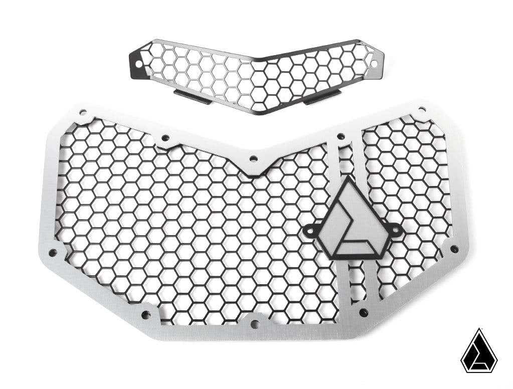 The Assault Industries Hellfire v2 Front Grill for Can-Am Maverick X3 features two metal mesh grilles with a hexagonal pattern and angular edges. The larger grille has a geometric triangular logo; the smaller is similarly designed above it.