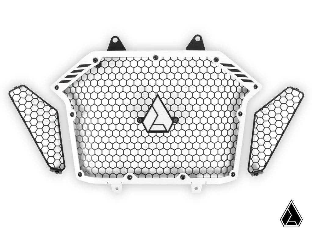 The Assault Industries Polaris RZR Pro XP Stinger Grille is a white honeycomb-patterned radiator guard with two matching side pieces, all featuring black borders, black mounting tabs, and a triangle logo at the center and bottom right.