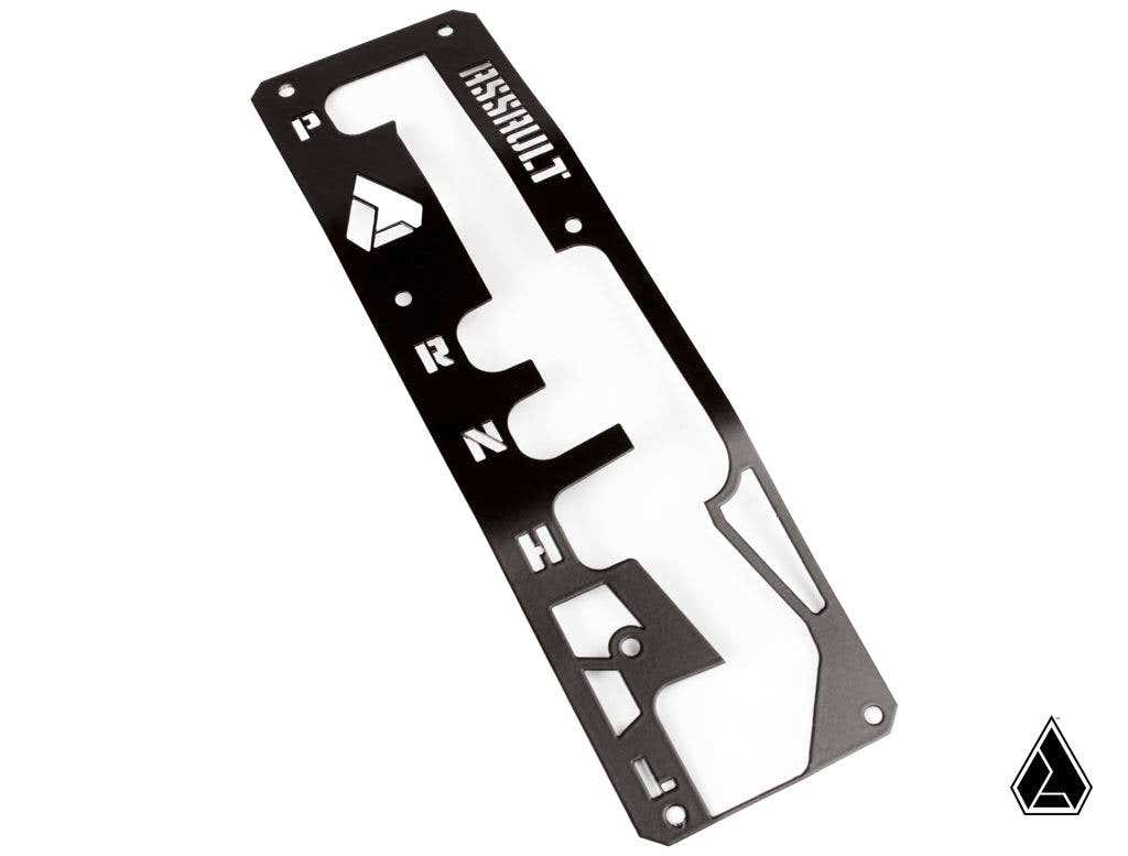 A black metal Assault Industries Shifter Gate Panel Kit for Can Am Maverick X3 with P R N H L cutouts, geometric logo designs, labeled KASSHULT at the top, multiple screw holes, white background, and a small triangle logo bottom right.