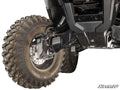 Close-up of a Honda Rancher 4 Portal Gear Lift installed on the front left wheel, showcasing deep-tread tires with mud, visible black chassis and suspension components. The SuperATV logo is displayed in the lower right corner.